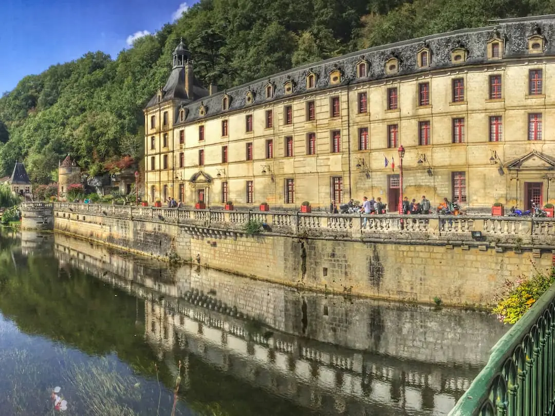 A long stone building with grey roof looks out over a river