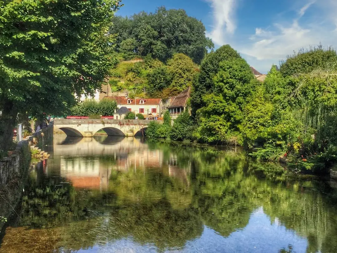 A bridge stretches across a river with its reflection and surrounding trees in the water