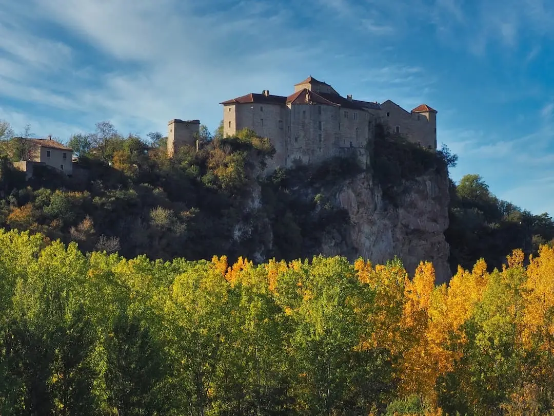 A stone village sits atop a hill with autumnal trees in the foreground