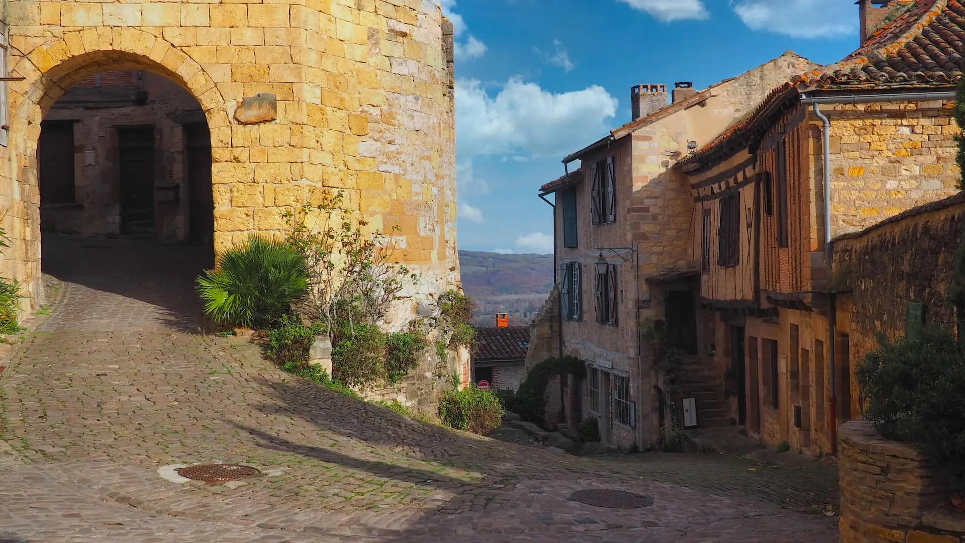 A stone archway on the left leads from the top of a hill of medieval buildings