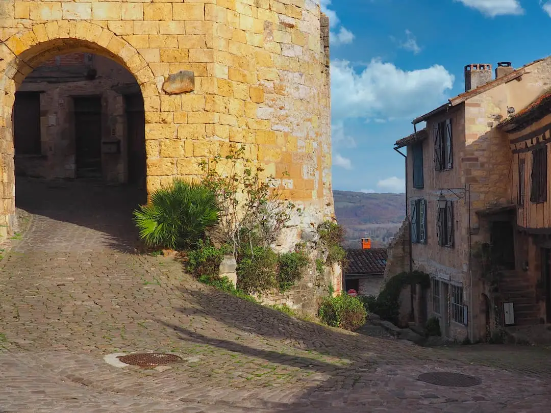 A stone archway on the left leads from the top of a hill of medieval buildings