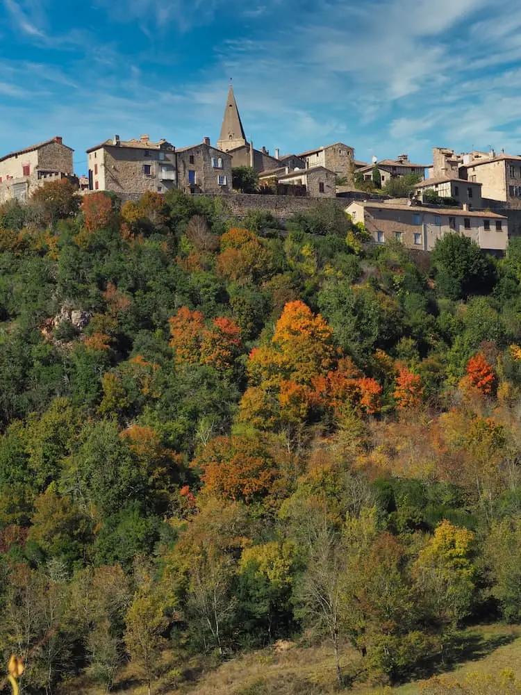An old stone-built town looks out over a hillside of autumnal trees