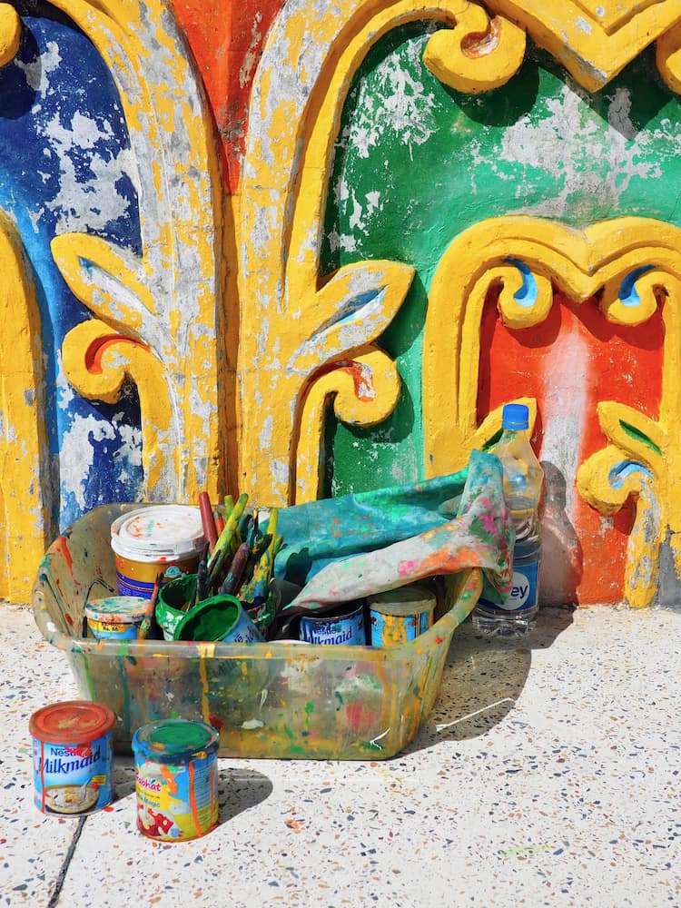 Pots of paint in front of a building wall coloured red, blue, green and yellow