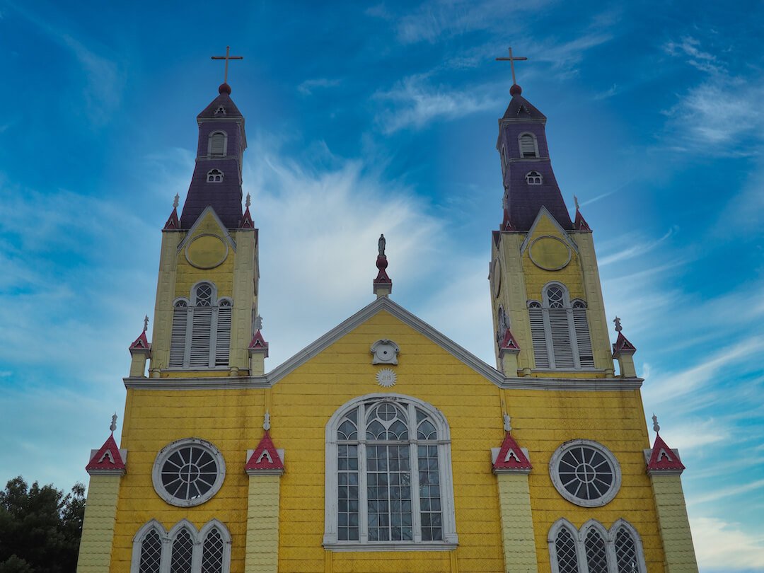 A yellow wooden church with two towers on each side with a blue sky behind