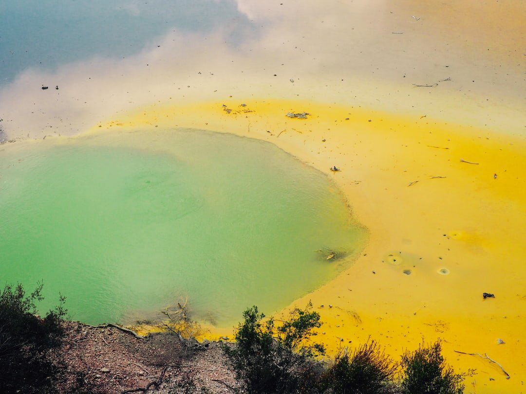 A pool of water coloured green and yellow with a reflection of blue sky and clouds