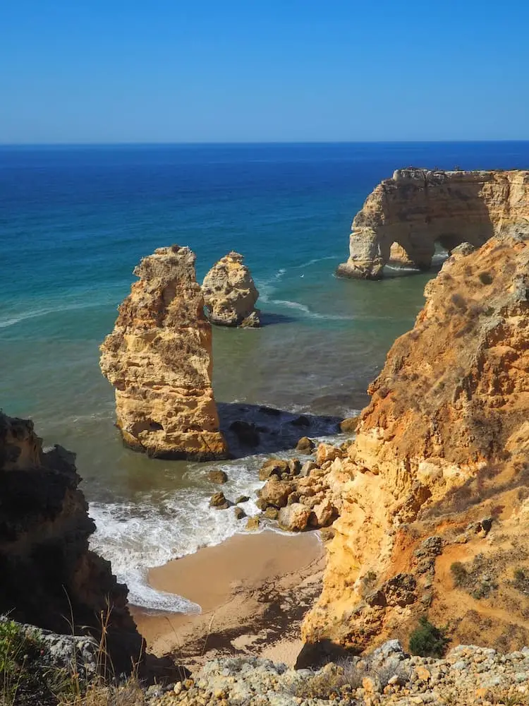 A beach sandwiched between offshore rocks and cliffs