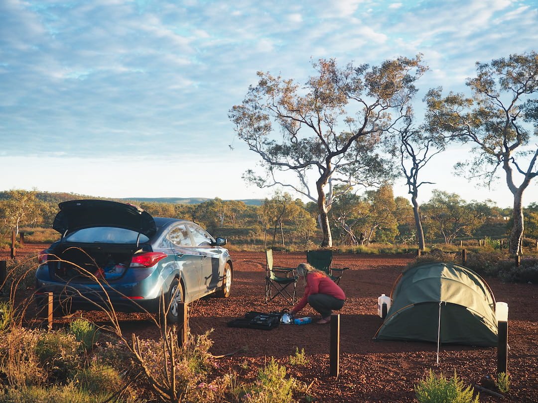 Nicky prepares a campfire in between a car and a small tent