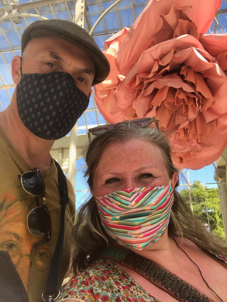 Ian and Nicky wearing masks with a large decorative flower in the background
