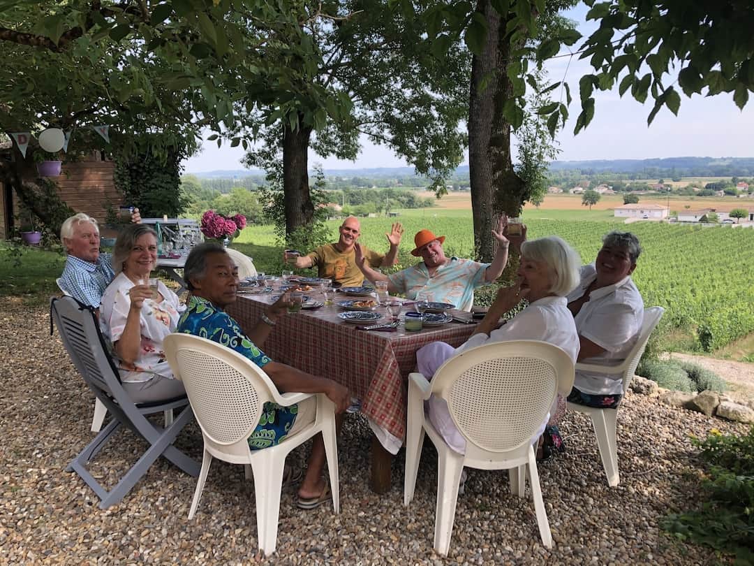 A group of people sit around an outdoor table and chairs overlooking a vineyard