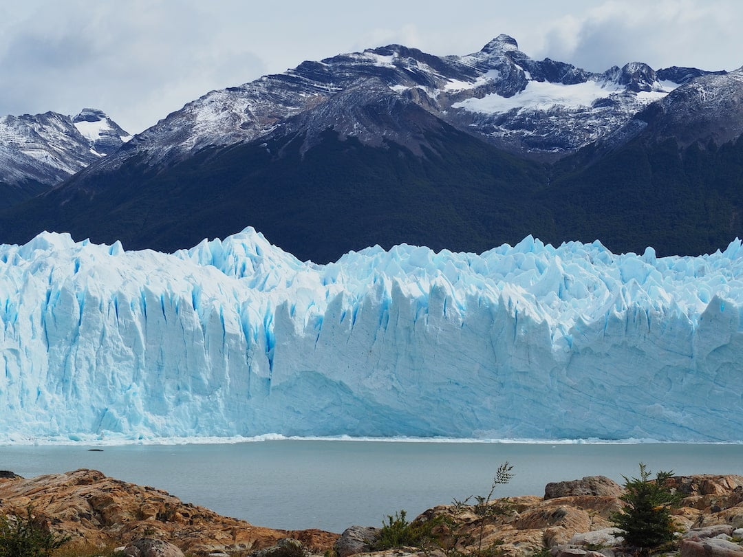 A wall of ice behind an expanse of water in front and mountains in the background
