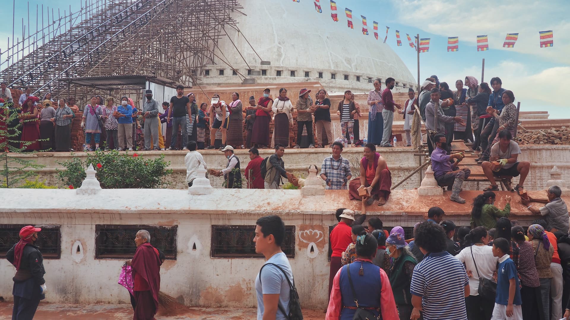 People standing around the Boudha Stupa passing building materials to one another