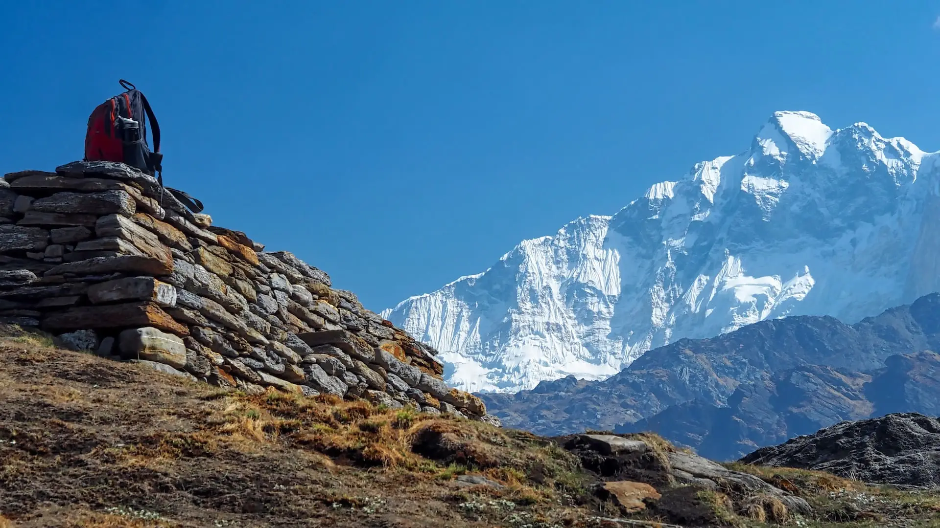 An orange backpack on a wall (left) and white snow-capped mountains (right)