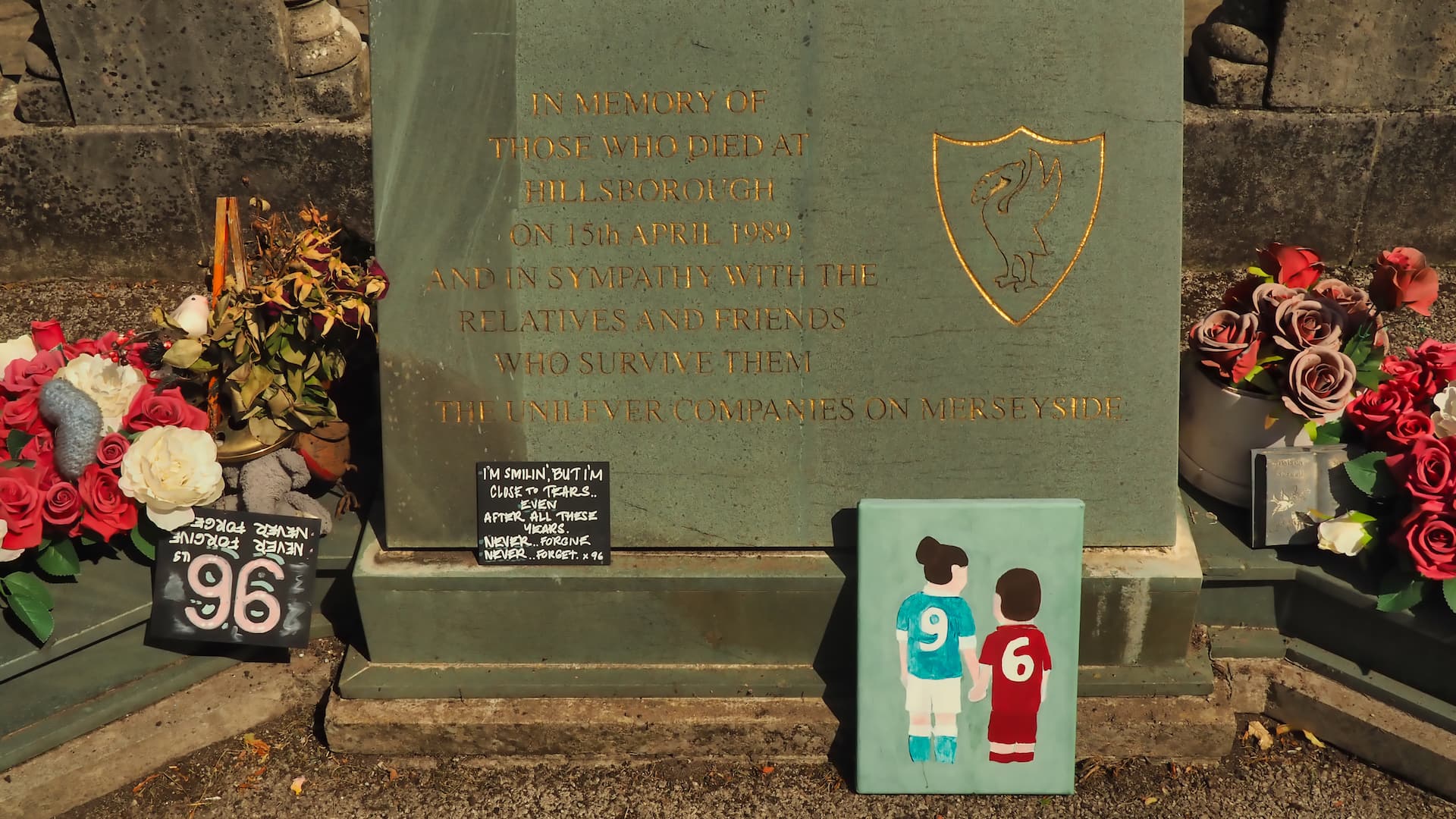 Flowers places on each side of a stone plaque and a drawing of two figures in blue and red football kits