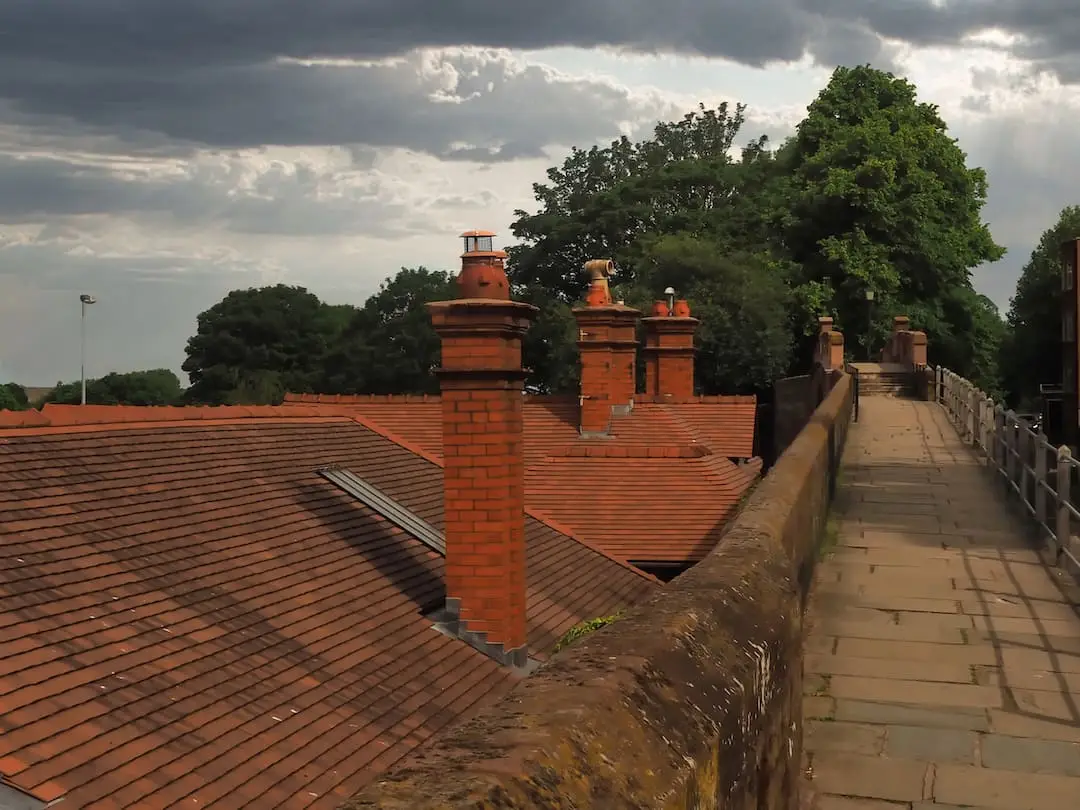 Red rooftops with chimneys to the left, a wall and footpath to the right