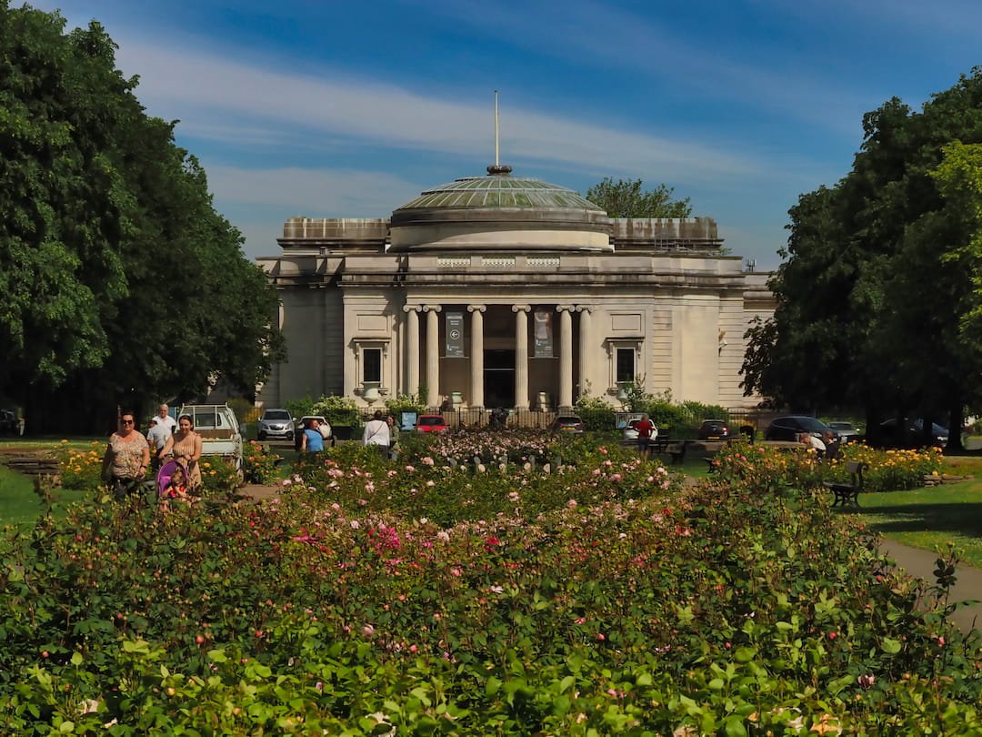 A building with pillars in the background and a flower garden in the foreground leading to it