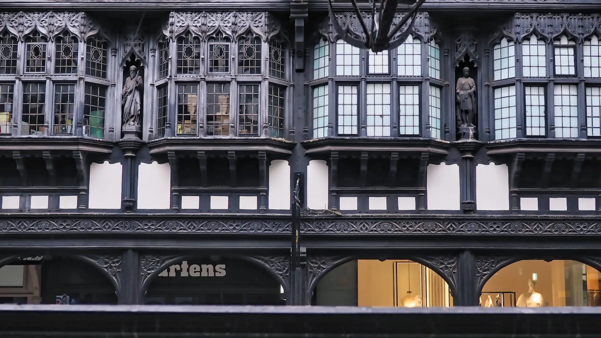 A black and white half-timbered facade with four windows and two statues