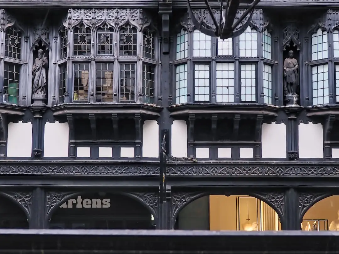 A black and white half-timbered facade with four windows and two statues