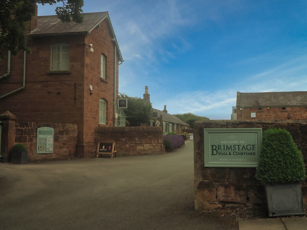 A sign for Brimstage Hall with sandstone buildings behind