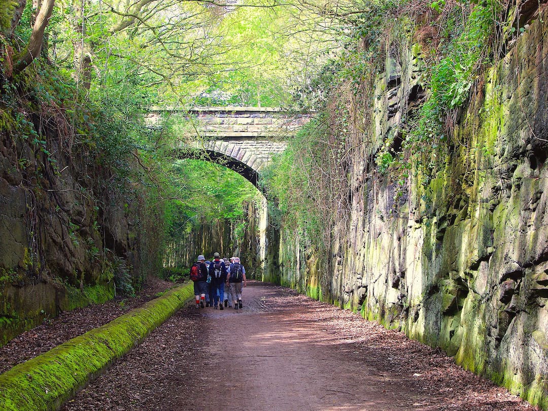 A footpath runs between two stone walls, with a stone bridge running across it in the background