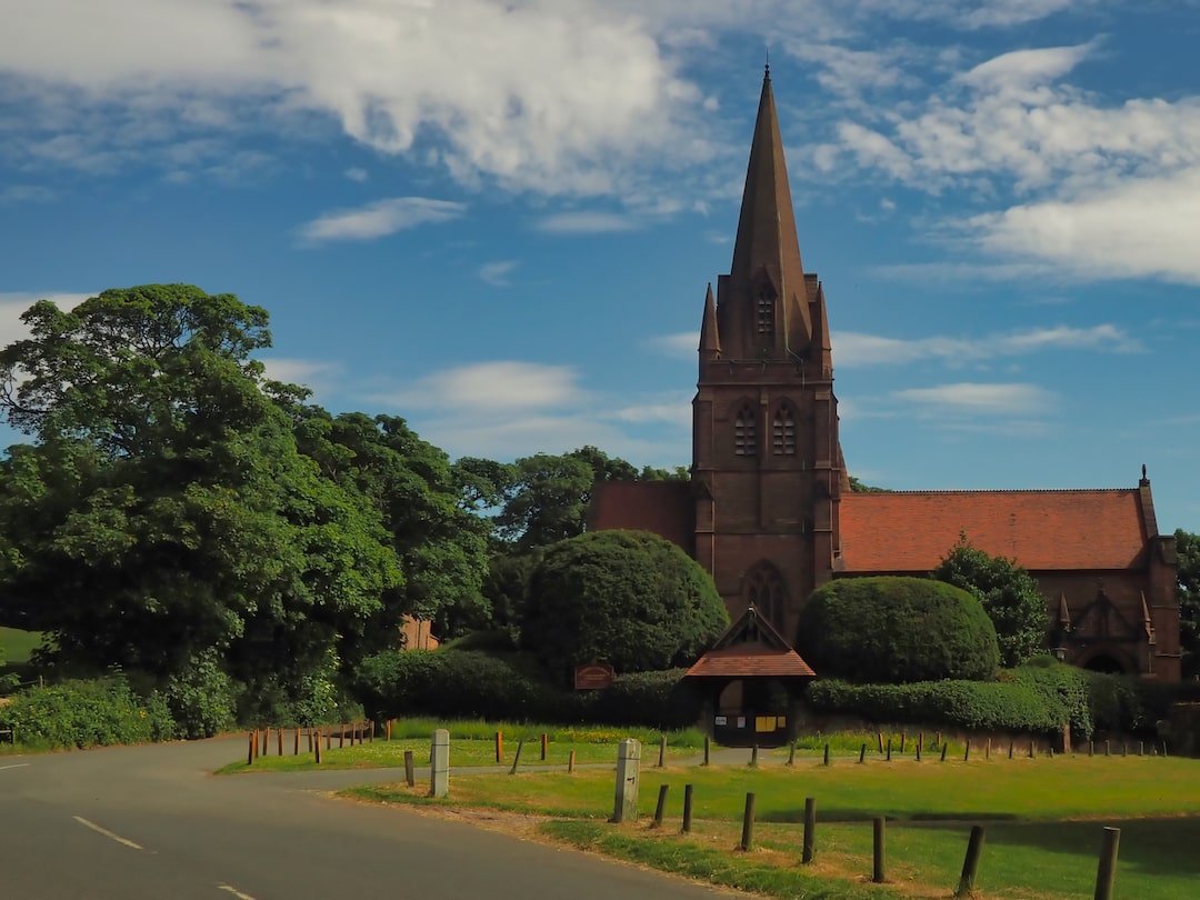 A red sandstone church with a spire, surrounded by trees