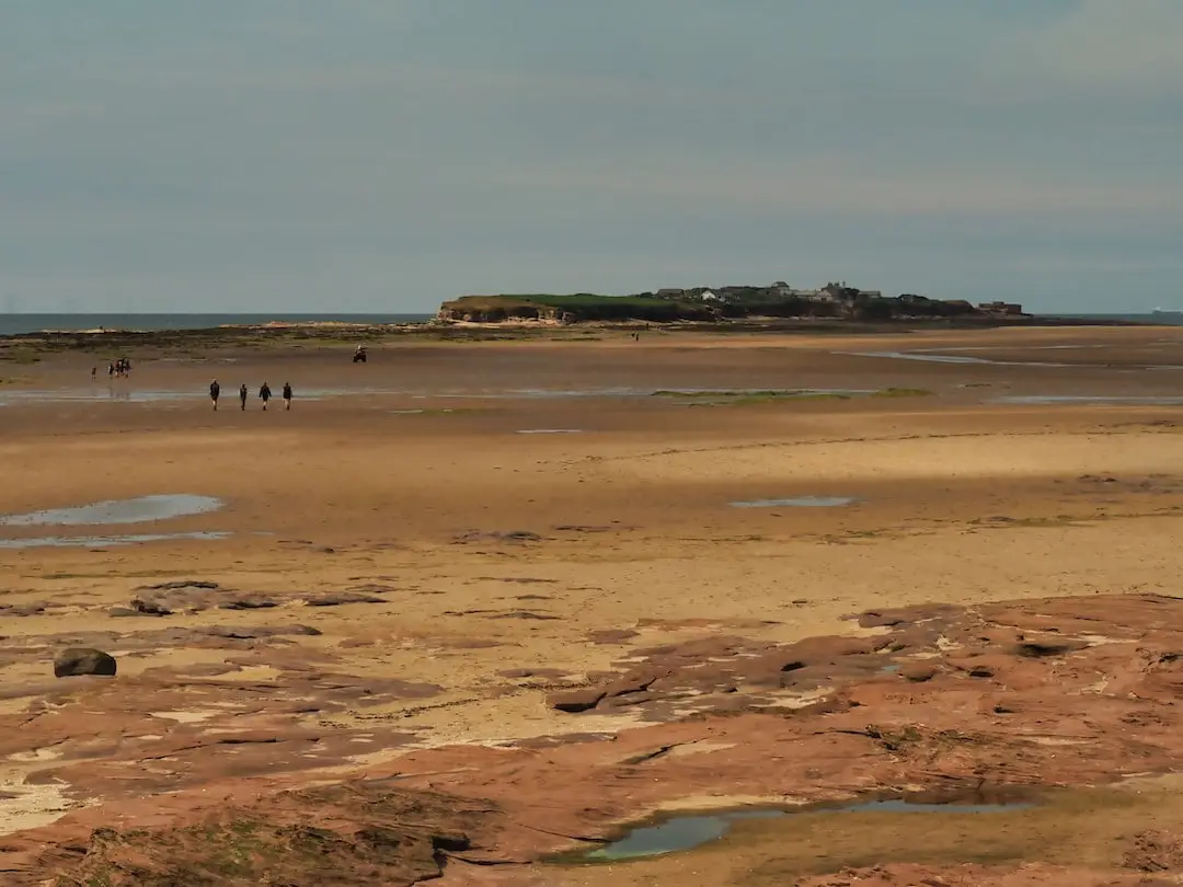 Sandstone rocks in the foregrounds beach in the middle ground and an island in the background