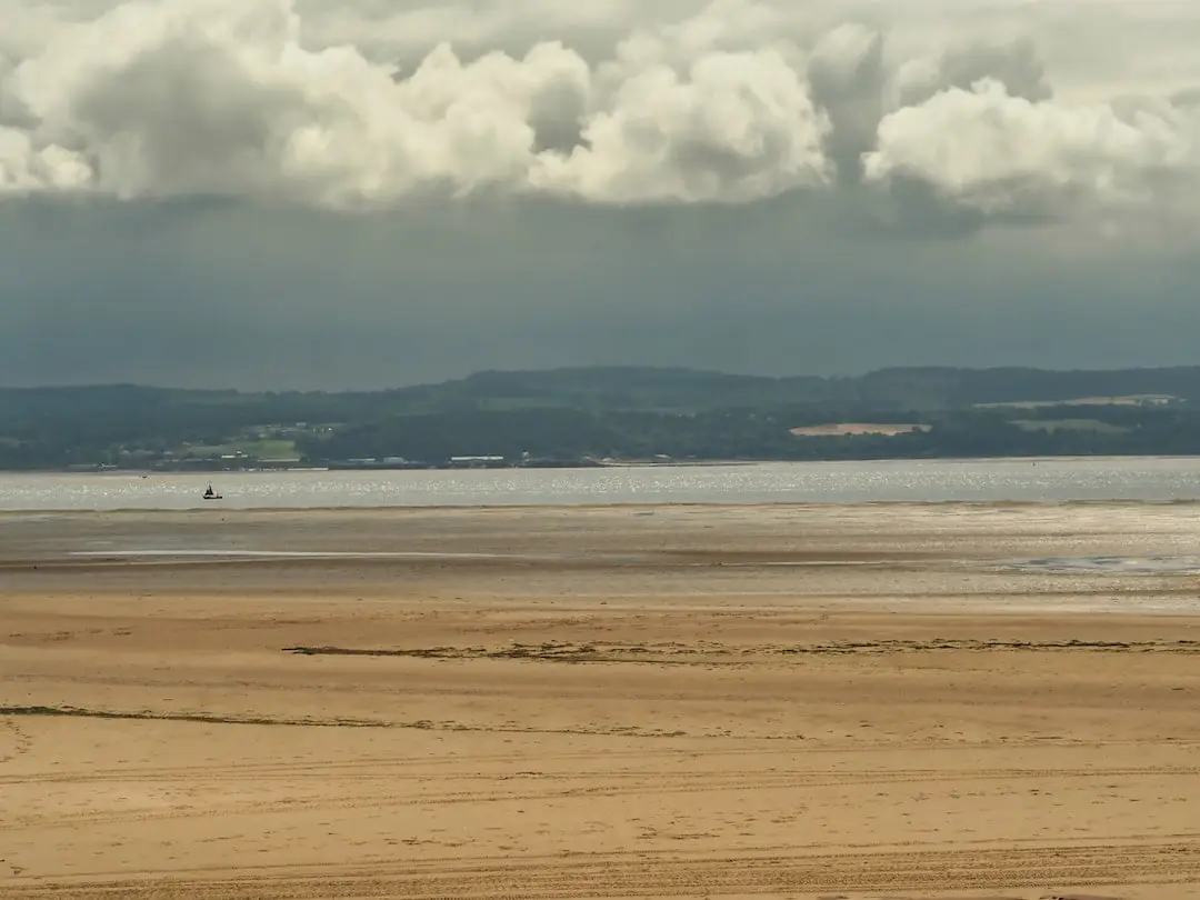 A beach in the foreground with mountains and dark clouds in the background