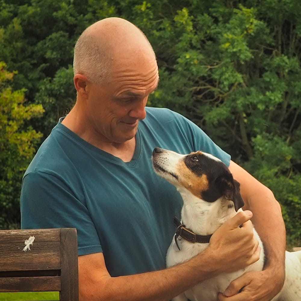 A man in a blue shirt holds a small dog