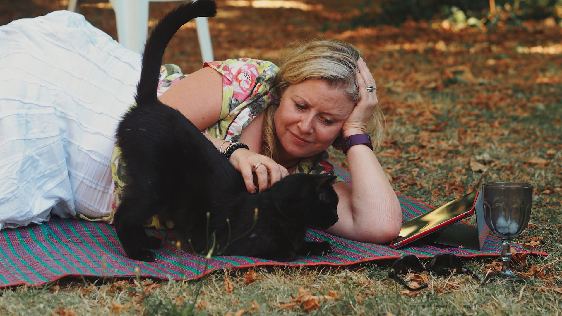 A woman lies beside and strokes a black cat