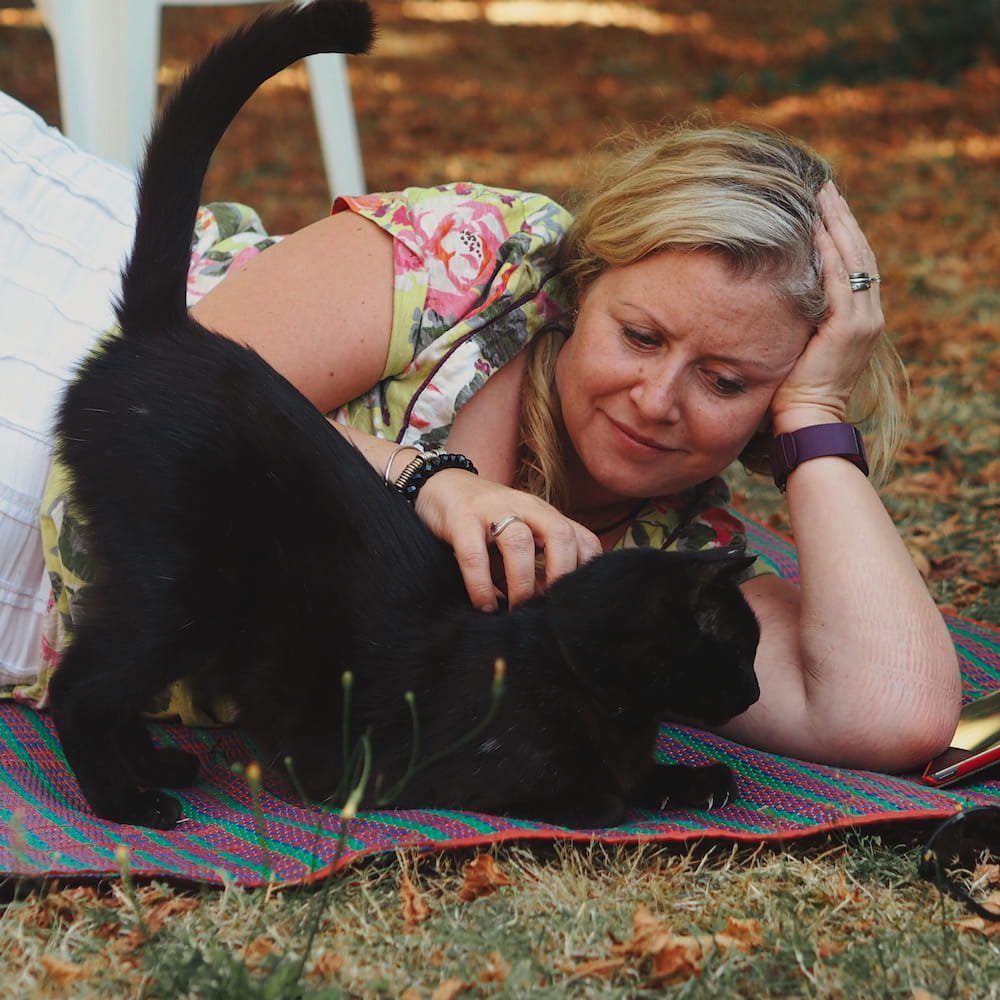 A woman lies beside and strokes a black cat