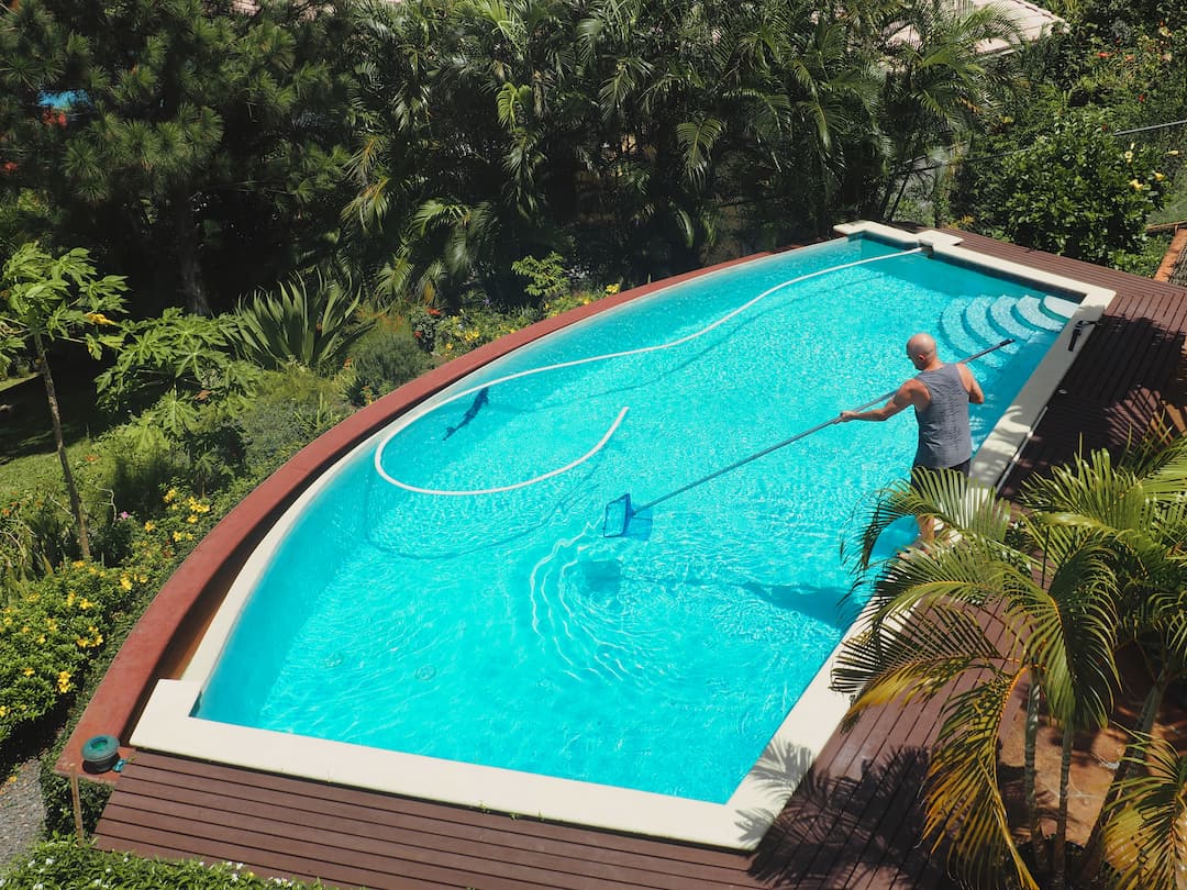 A man cleans a swimming pool of debris with a net on a long pole