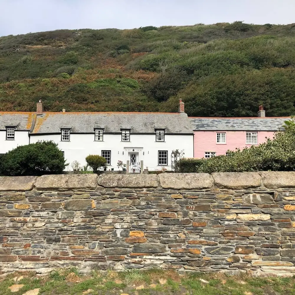 Boscastle - Valency Row A stone wall in the foreground with pink and white coloured cottages in the background