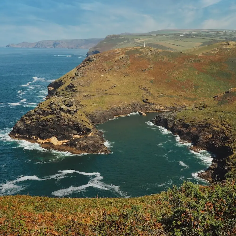 Boscastle - view from lookout A green-covered headland wraps around blue water of the sea, with hills in the background