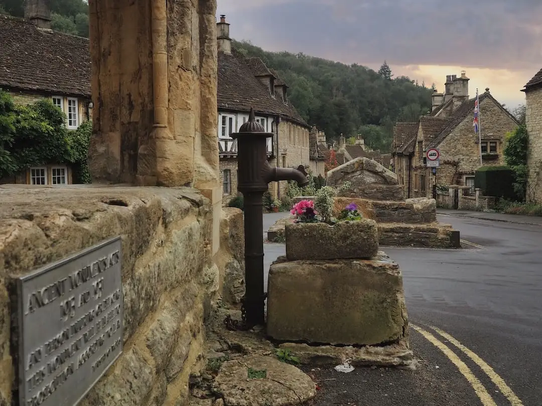 A stone building in the middle of a road with a black water pump