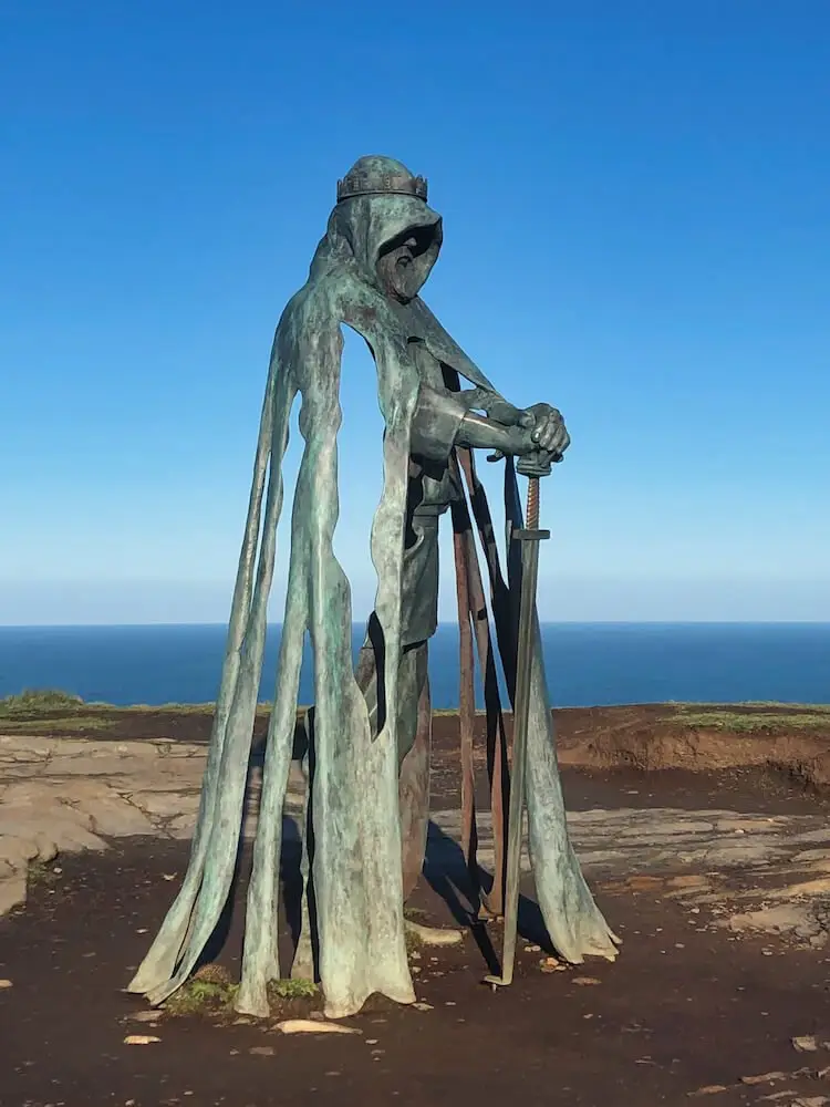 King Arthur Statue Tintagel A statue of a man holding a sword on a clifftop with the sea in the background