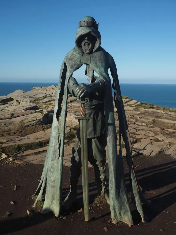 Tintagel - King Arthurs Statue. A statue of a man holding a sword on a clifftop with the sea in the background