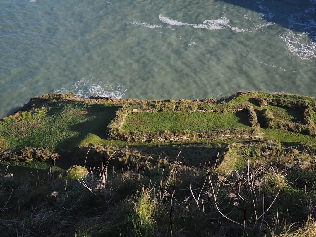 Tintagel - settlement ruins A patchwork of ancient building foundations and green grass sit sit on a hillside overlooking the sea