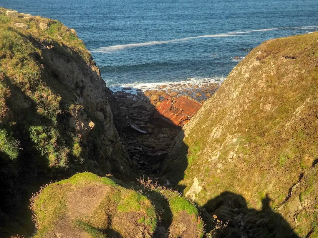 The remains of a shipwreck lies on a beach between two cliffs