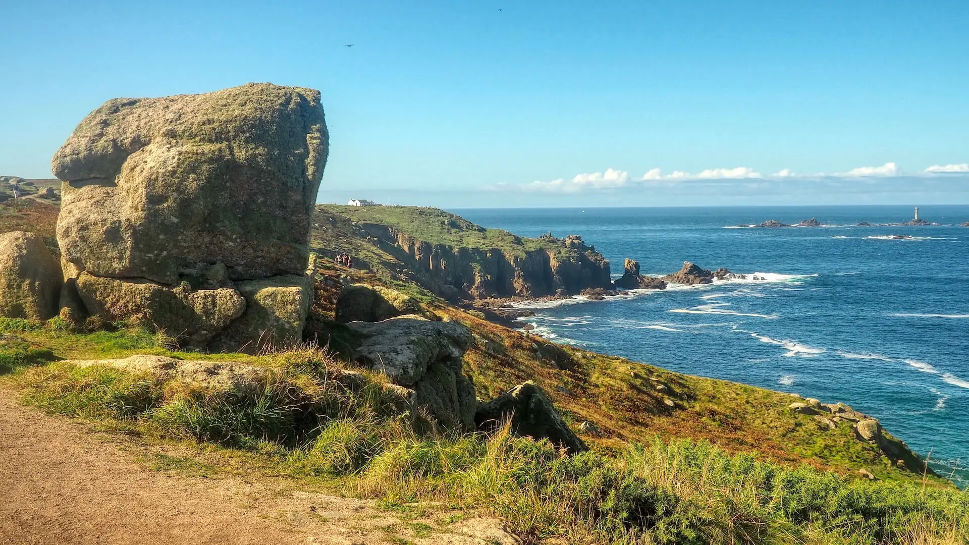 On the Sennen Cove to Lands End Walk, a woman stands on a rock and turns to the camera
