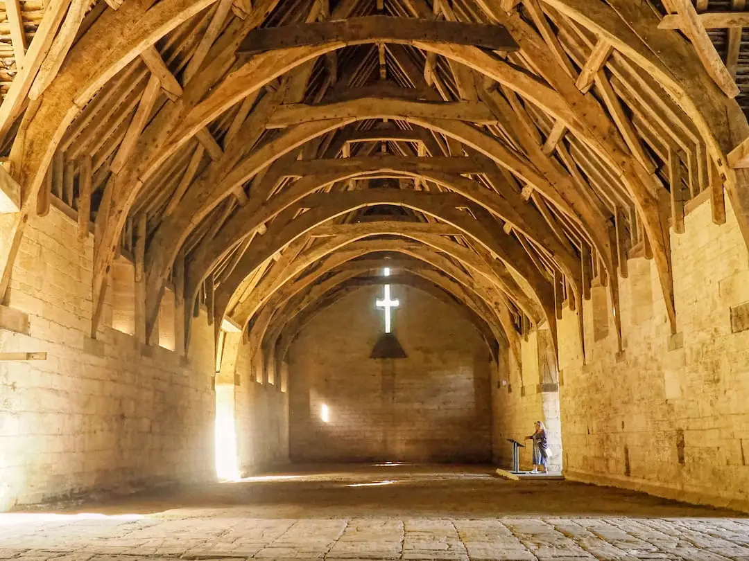 A stone barn interior with a wooden ceiling and cross window on the far wall