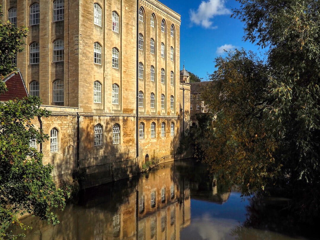 A stone building with many windows is reflected in the river below
