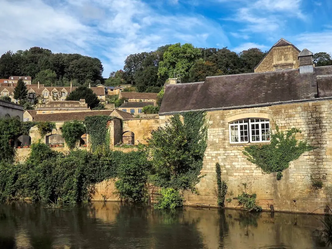 Stone buildings beside a river and covered with green foliage