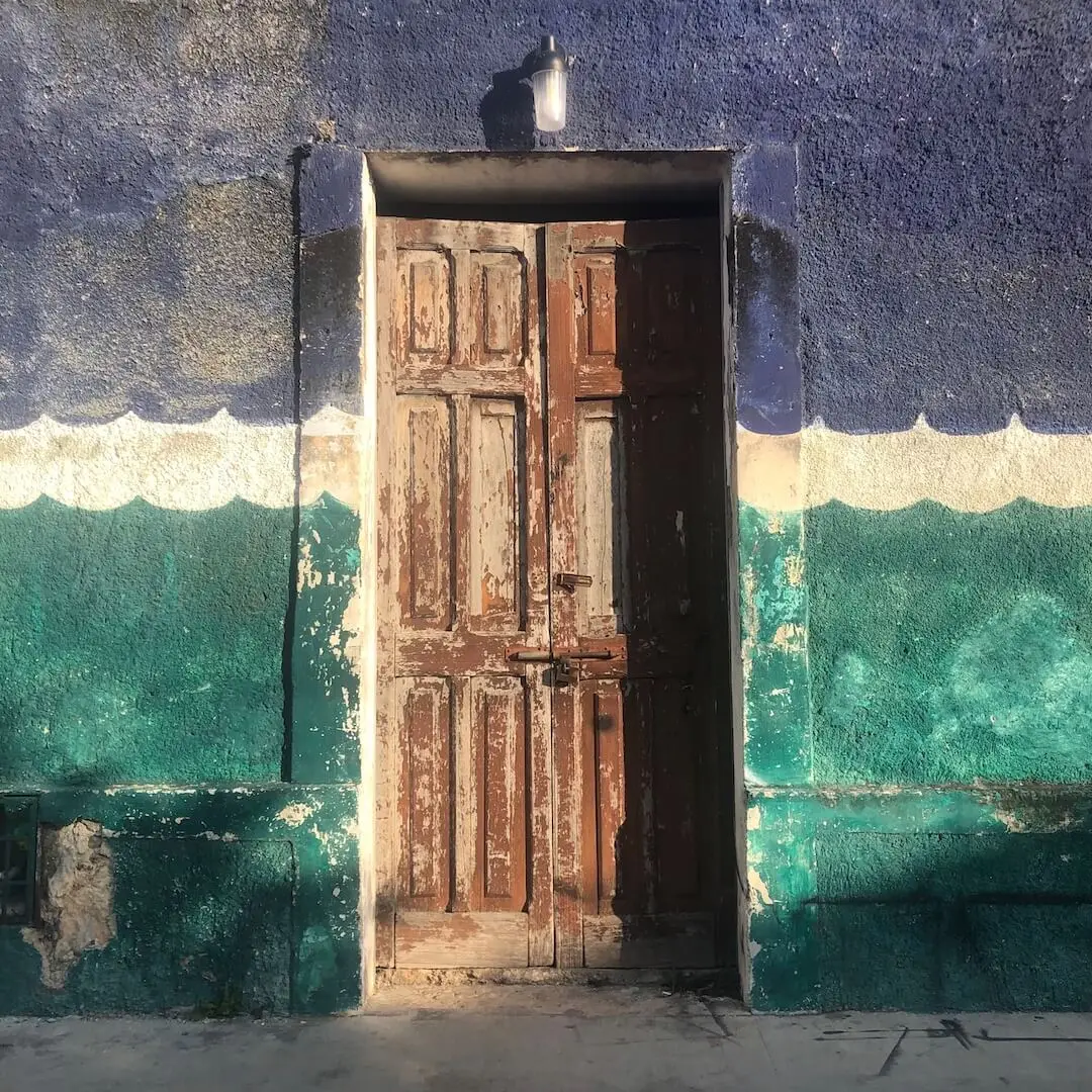 A brown door cuts through a blue, green, and cream coloured building