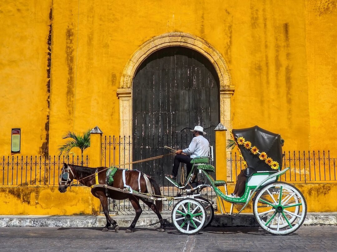 A horse pulls a cart and driver in front of a yellow church