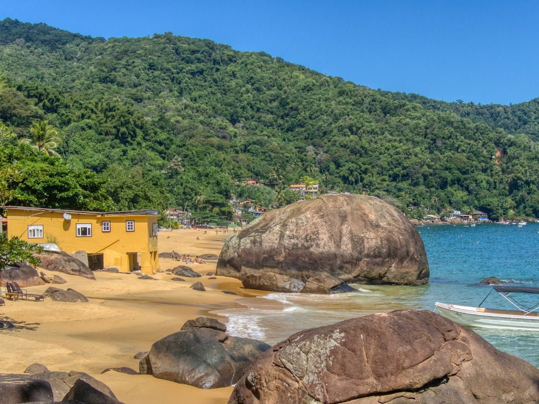 Large granite boulders and yellow building on a golden beach