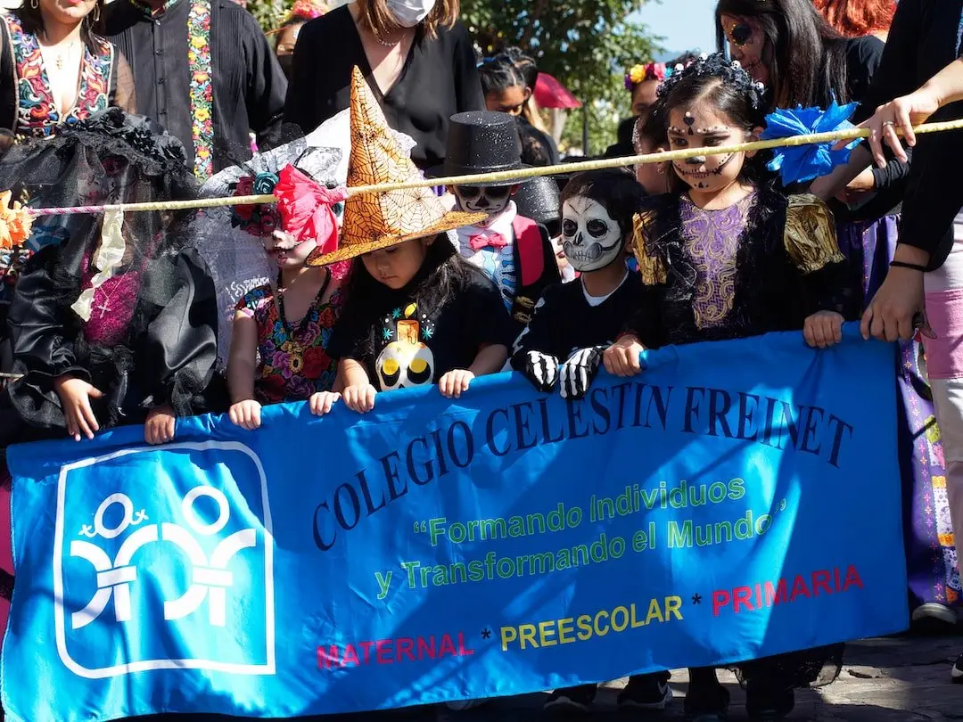 A childrens parade for Day of the Dead Oaxaca A row of children with their faces painted stand behind a blue banner