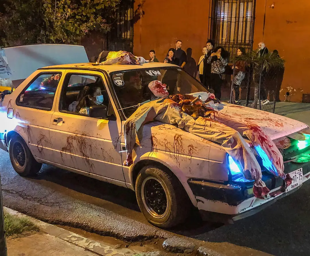 Car convoy duirng Oaxaca Day of the Dead A white car is "decorated" with a gruesome looking dummy on its bonnet