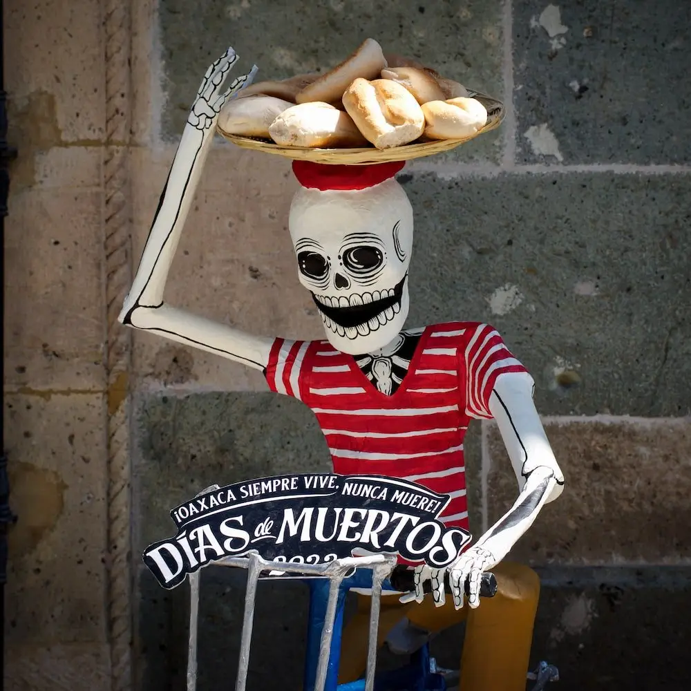 Day of the Dead skeleton in Oaxaca A skeleton in a red hooped shirt sits on a bicycle with a basket of bread on its head