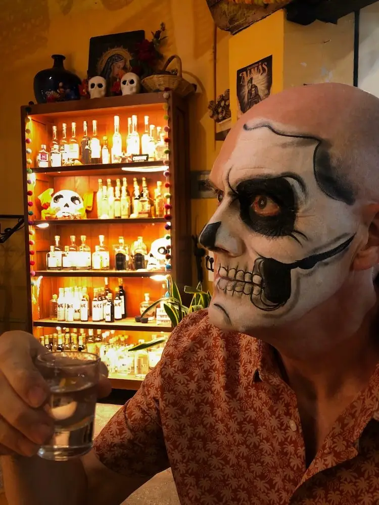 Ian with face painted for Day of the Dead in Oaxaca Ian in face paint drinks a mezcal in a bar