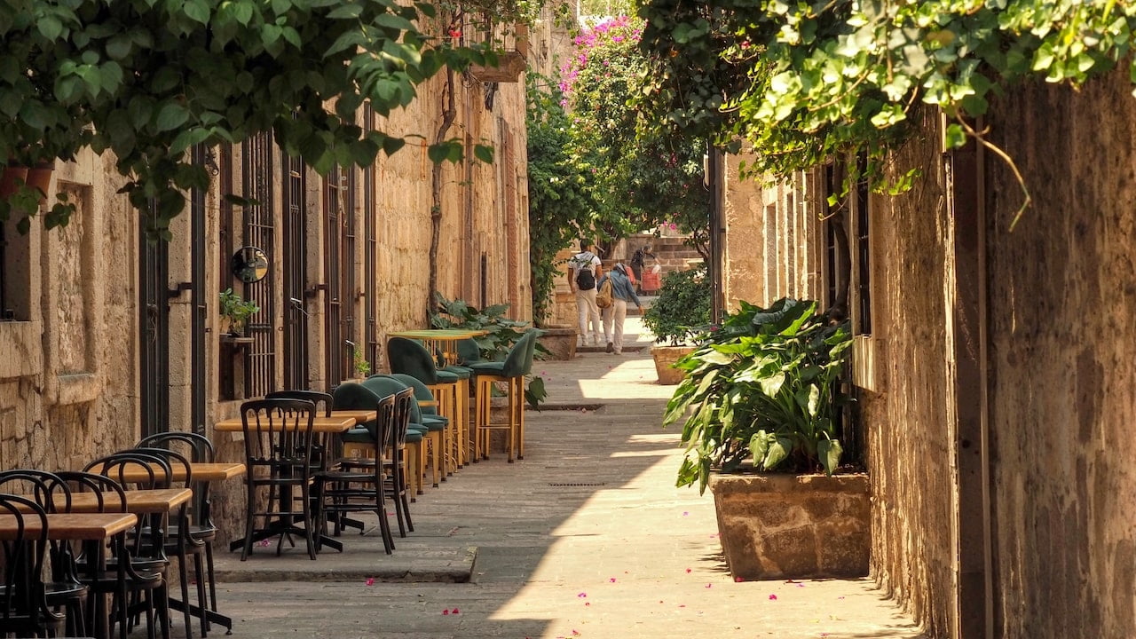 A narrow street with outdoor tables and chairs, potted plants etc