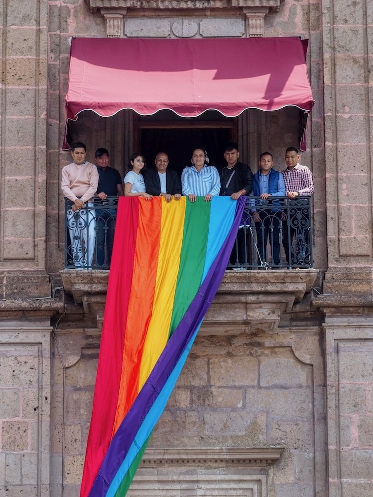 People drape a rainbow flag from an office balcony